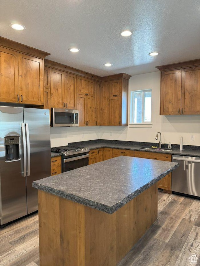kitchen with a sink, appliances with stainless steel finishes, dark countertops, light wood-style floors, and brown cabinetry