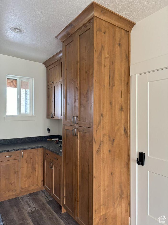 kitchen with dark wood-type flooring, a textured ceiling, brown cabinetry, and dark countertops