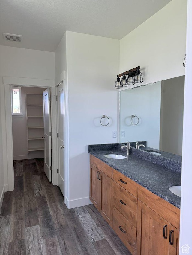 full bathroom featuring visible vents, wood finished floors, a sink, double vanity, and baseboards