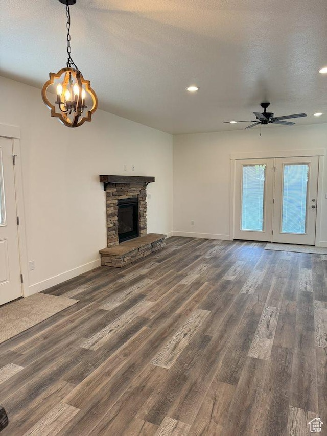 unfurnished living room with ceiling fan with notable chandelier, a fireplace, a textured ceiling, wood finished floors, and baseboards
