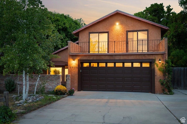 view of front of home featuring an attached garage, fence, stucco siding, a balcony, and driveway