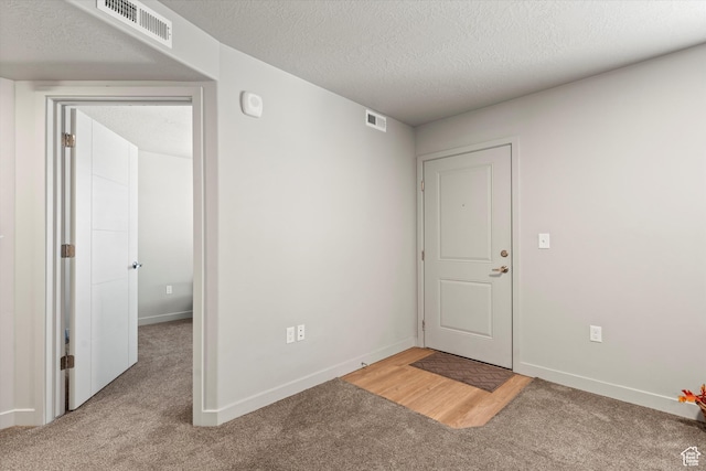 carpeted empty room featuring a textured ceiling, visible vents, and baseboards