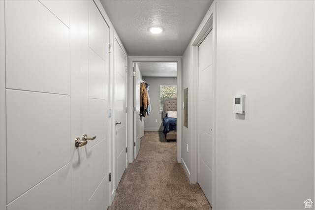 hallway featuring light carpet, a textured ceiling, and baseboards