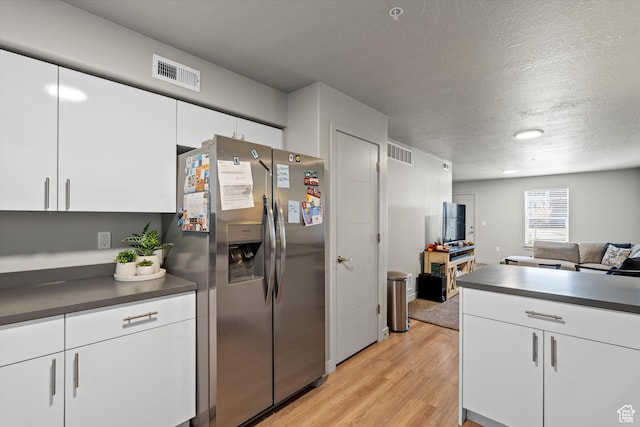 kitchen with dark countertops, light wood finished floors, stainless steel fridge, and visible vents