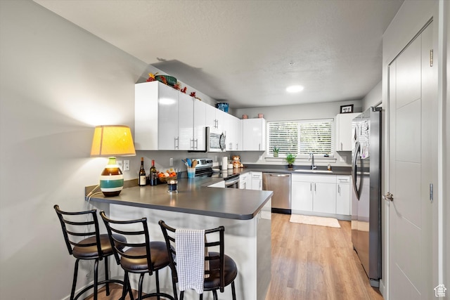 kitchen featuring light wood finished floors, a sink, a peninsula, dark countertops, and stainless steel appliances