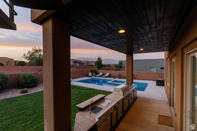 3318 S Red Rock Way, Hurricane, UT 84737 - pool at dusk with a patio, a fenced in pool, a fenced backyard, a lawn, and an outdoor kitchen