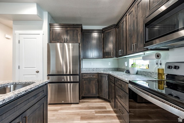 668 S 400 E, Clearfield, UT 84015 - kitchen with appliances with stainless steel finishes, dark brown cabinets, light stone counters, light wood-style flooring, and a textured ceiling