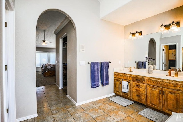 full bath featuring double vanity, baseboards, ensuite bathroom, ceiling fan, and a sink