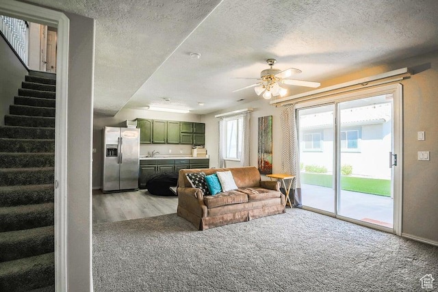 living area featuring stairs, baseboards, ceiling fan, a textured ceiling, and carpet flooring