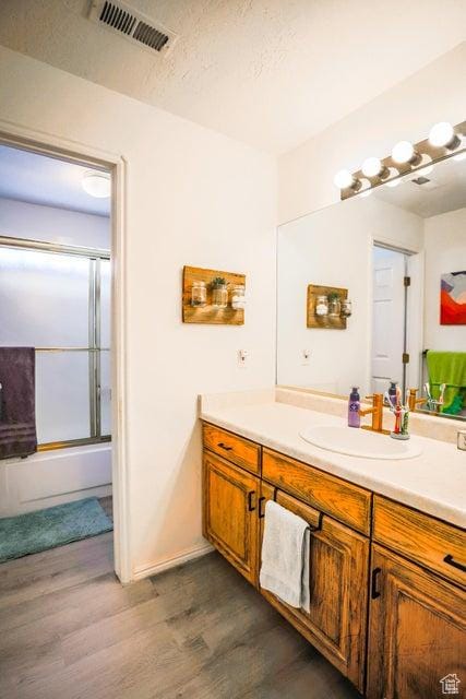 full bath featuring enclosed tub / shower combo, visible vents, wood finished floors, and vanity