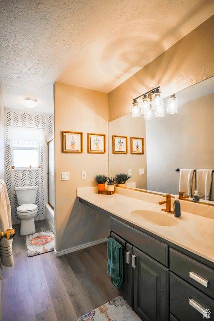 bathroom with a textured ceiling, wood finished floors, vanity, toilet, and shower / bath combination with glass door