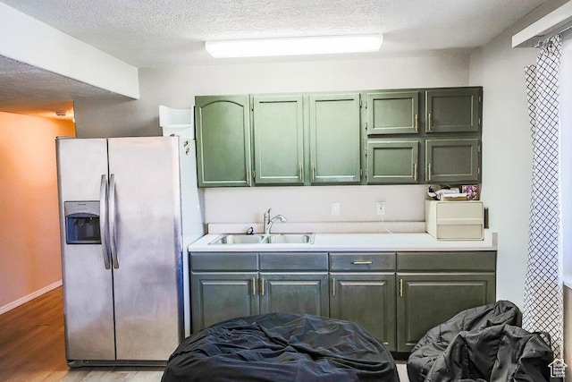 kitchen with light wood-style floors, stainless steel fridge, light countertops, a sink, and green cabinets