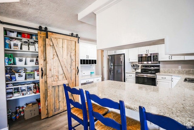 kitchen featuring white cabinetry, light stone countertops, appliances with stainless steel finishes, and a barn door