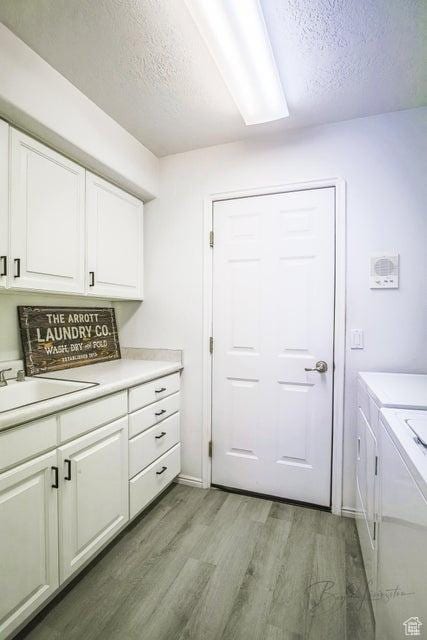 laundry room with cabinet space, independent washer and dryer, a sink, light wood-style floors, and a textured ceiling