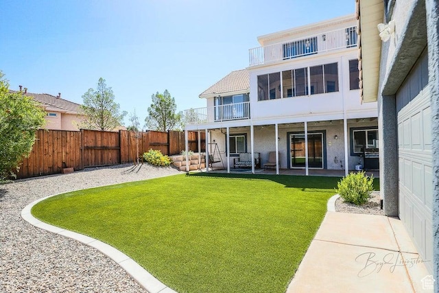 rear view of house with a lawn, a patio area, a fenced backyard, a balcony, and stucco siding