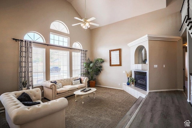 living area featuring ceiling fan, a tile fireplace, wood finished floors, high vaulted ceiling, and baseboards