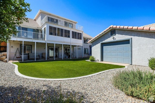 back of property with a lawn, a garage, a balcony, and stucco siding
