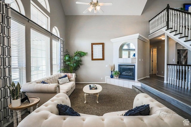 living area with baseboards, ceiling fan, a fireplace, and a towering ceiling