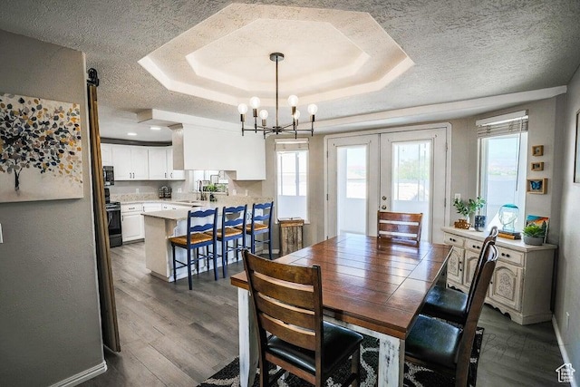 dining room with a textured ceiling, a notable chandelier, dark wood finished floors, and a raised ceiling