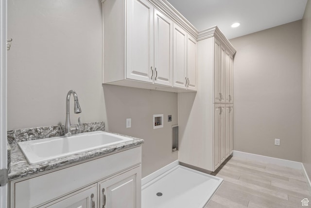 washroom with light wood finished floors, washer hookup, a sink, electric dryer hookup, and cabinet space
