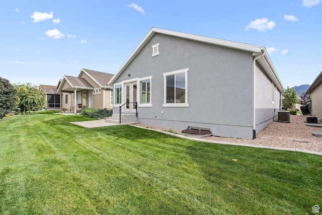 rear view of property with stucco siding, central air condition unit, and a yard