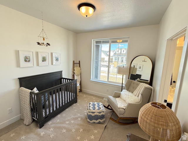carpeted bedroom featuring baseboards, a textured ceiling, and a crib