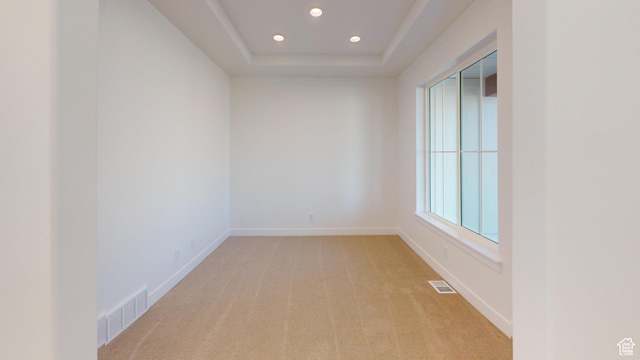empty room featuring visible vents, a raised ceiling, light colored carpet, and baseboards