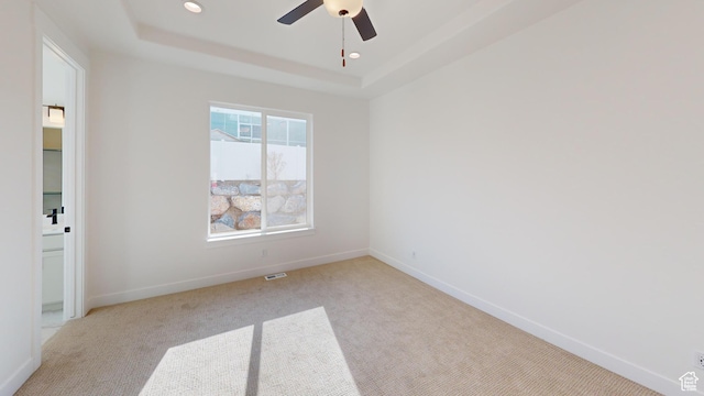 unfurnished room featuring a raised ceiling, recessed lighting, baseboards, and light carpet