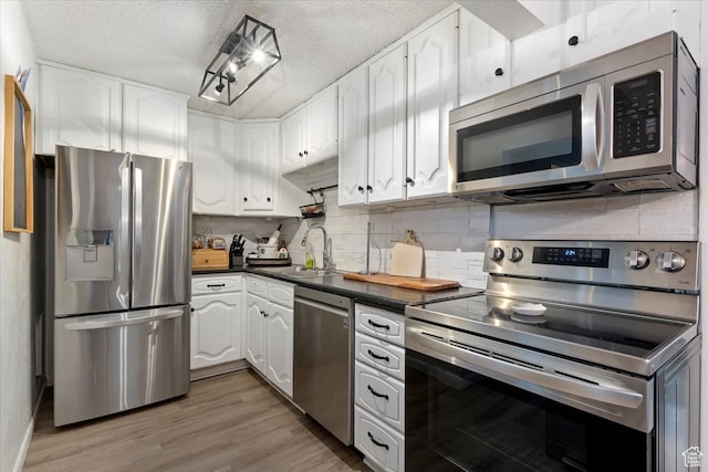 kitchen featuring sink, tasteful backsplash, wood-type flooring, white cabinetry, and appliances with stainless steel finishes