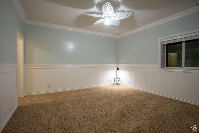 carpeted spare room with wainscoting, crown molding, and a ceiling fan