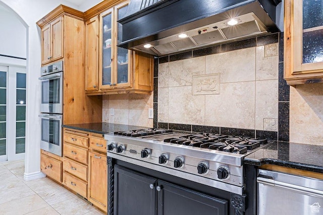 kitchen with premium range hood, dark stone counters, backsplash, appliances with stainless steel finishes, and glass insert cabinets