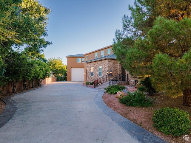 view of front of home featuring concrete driveway, stucco siding, fence, stone siding, and a garage
