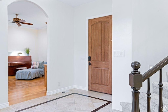 foyer with arched walkways, baseboards, stairway, and ceiling fan