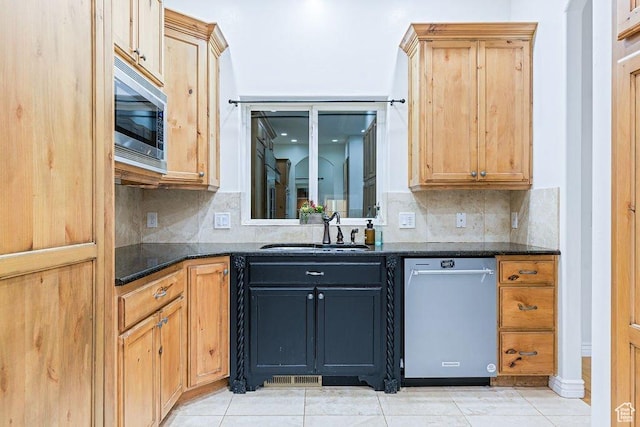 kitchen featuring light tile patterned floors, stainless steel appliances, decorative backsplash, dark stone counters, and a sink