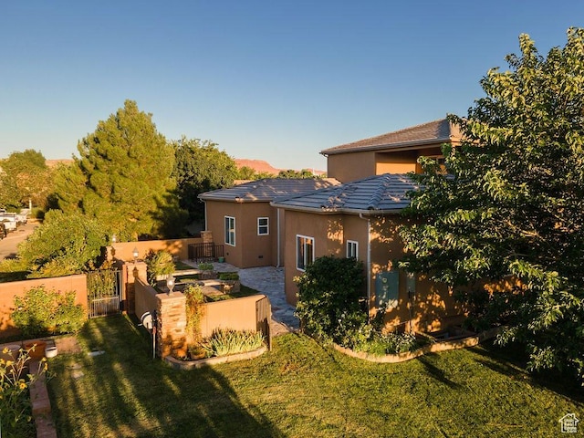 back of property featuring a gate, a patio area, stucco siding, fence, and a yard