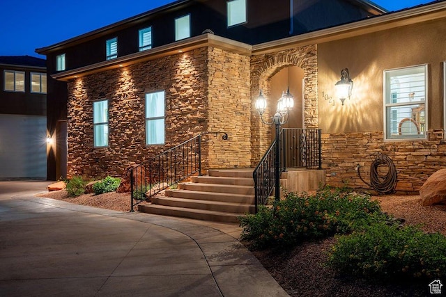 doorway to property featuring stone siding, concrete driveway, and stucco siding