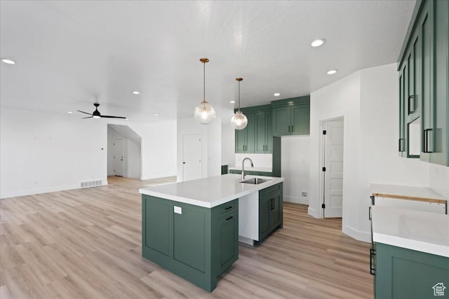kitchen featuring green cabinets, an island with sink, visible vents, and a sink