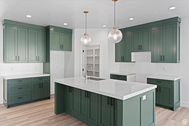 kitchen featuring green cabinetry, a sink, pendant lighting, a kitchen island with sink, and light wood-style floors