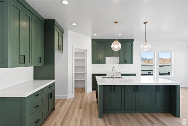 kitchen featuring green cabinets, a kitchen island with sink, a sink, and light wood-type flooring