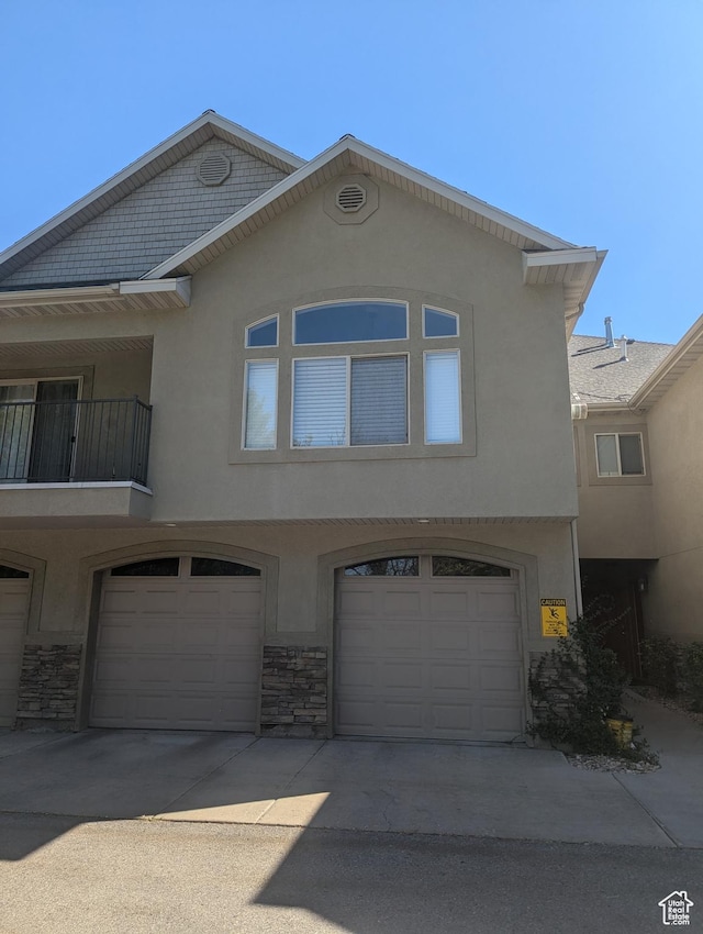 view of front facade with stucco siding, an attached garage, and stone siding