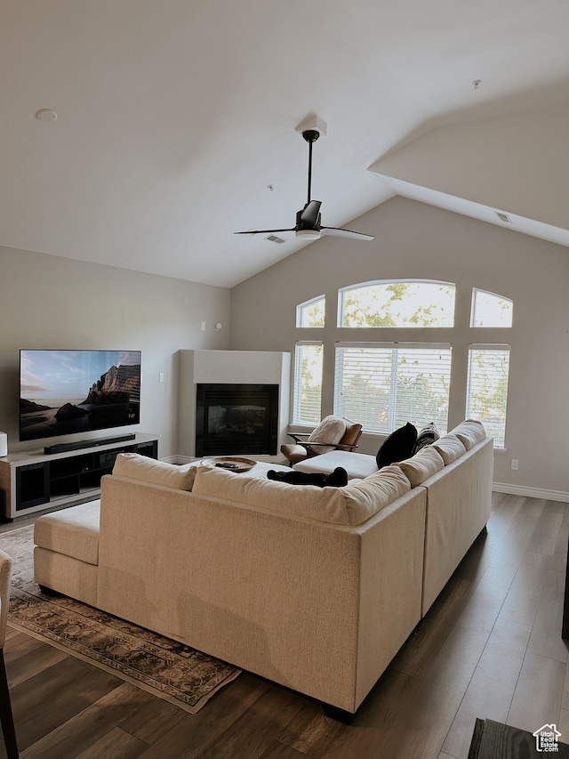 living area featuring lofted ceiling, visible vents, a ceiling fan, a glass covered fireplace, and wood finished floors