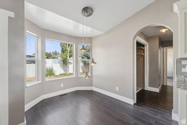 unfurnished dining area featuring visible vents, baseboards, arched walkways, and dark wood-style floors