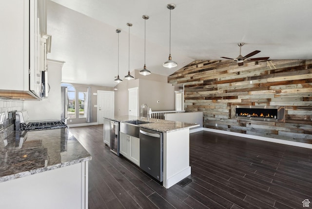 kitchen featuring dishwasher, ceiling fan, a sink, wooden walls, and a lit fireplace