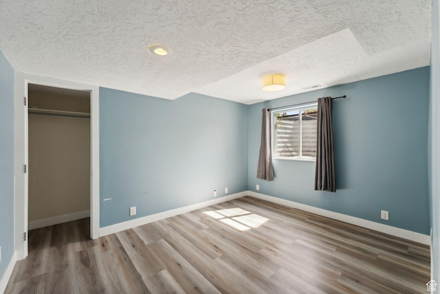 unfurnished bedroom with a closet, a textured ceiling, wood finished floors, and baseboards
