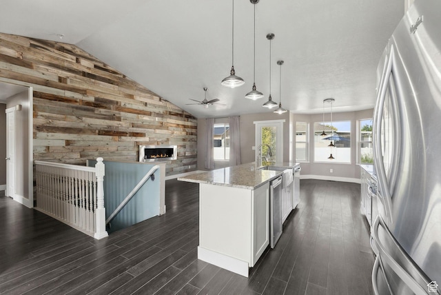 kitchen with a ceiling fan, open floor plan, appliances with stainless steel finishes, wooden walls, and lofted ceiling