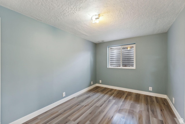 empty room featuring a textured ceiling, wood finished floors, and baseboards