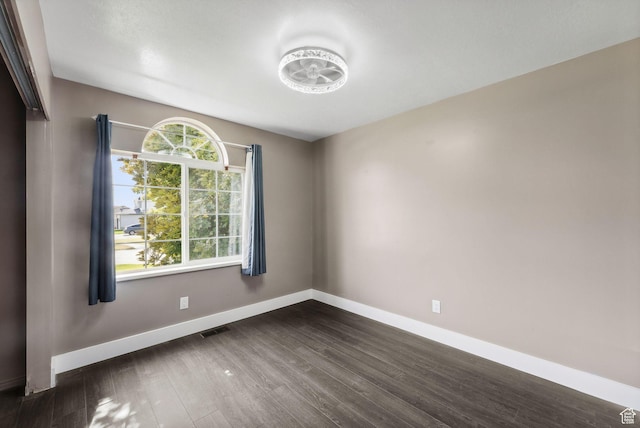 empty room featuring baseboards, visible vents, and dark wood-style floors