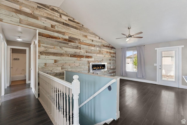 unfurnished living room featuring vaulted ceiling, a ceiling fan, dark wood-style floors, and wooden walls