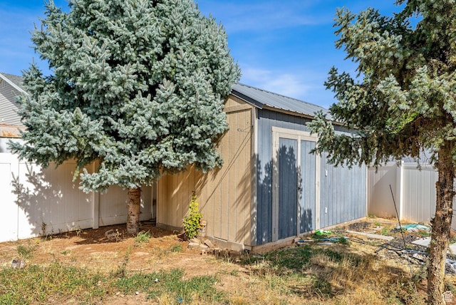 view of side of home featuring a storage shed, an outbuilding, fence, and metal roof