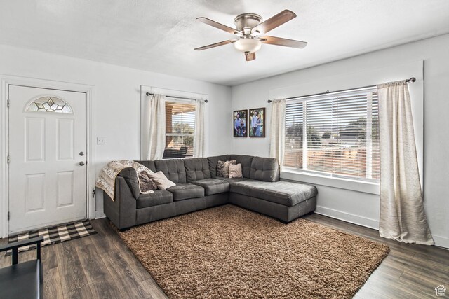 living area featuring baseboards, dark wood-type flooring, and a ceiling fan